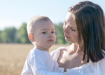 Fototapeta premium Young beautiful mother Holding child in her arms on nature in summer. Pretty woman looking with love on her baby son