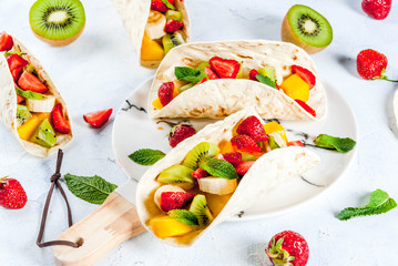 Summer snacks. Food for a party. Fruit tacos with strawberries, mangoes, bananas, chocolate, mint. On a light blue concrete table. Copy space