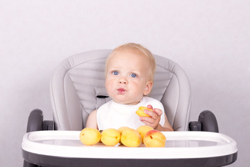 Funny toddler in a white bip eating an apricot