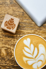 Coffee foam top view. Wooden cube with flower picture. Latte art basics.