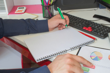 Man hand with pen, calculator and computer on wooden table. He is using his calculator and writing numbers down. Concept of accounting work