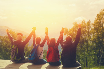 Group of team of friends sitting on top of a mountain, holding hands and rejoice, watching leaving sun behind the mountains - sunset.