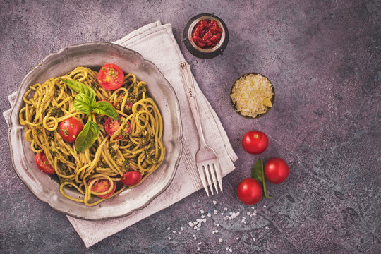 Pesto spaghetti pasta with cherry tomatoes on concrete background. Top view with copy space
