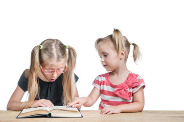 Fototapeta premium Two girls sitting at a desk studying an open book, pointing at her pointer isolated on white background
