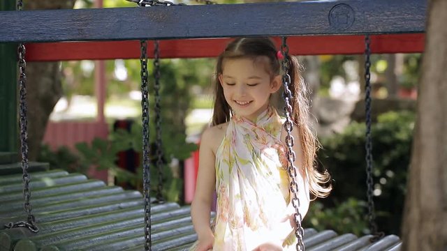 Little girl is sitting on the playground and is waving her hand looking at the camera