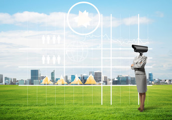Camera headed woman standing on green grass against modern cityscape