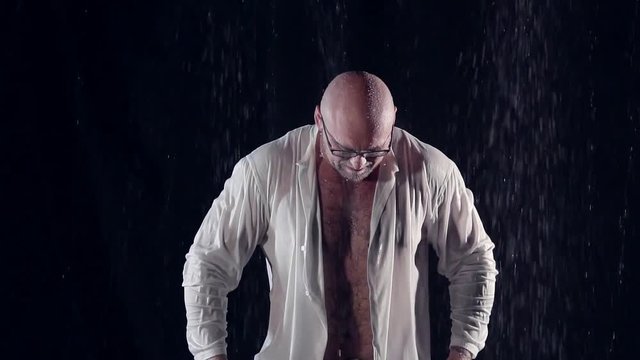 bald man with glasses got wet in the rain is touching his wet shirt. he has a bad mood