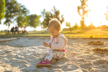 Fototapeta premium Fifteen months old baby girl playing in the sandbox in the sunset