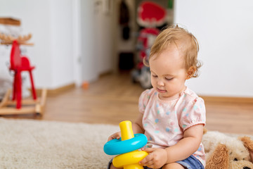 Fifteen months old baby girl playiing with her toys on the floor in the living room