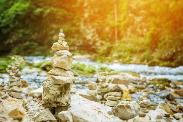 Balanced pyramide made of small rock stones on the shore of blue water of mountain river, with sun light leak