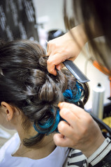 Fototapeta premium Closeup of a professional hairdresser's hands doing a hairstyle in a beauty salon. Model of a brunette with long hair. The concept of fashionable stylish hairstyle, professional work with hair.