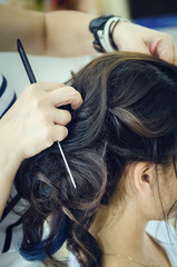 Fototapeta premium Closeup of a professional hairdresser's hands doing a hairstyle in a beauty salon. Model of a brunette with long hair. The concept of fashionable stylish hairstyle, professional work with hair.