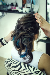 Naklejka premium Closeup of a professional hairdresser's hands doing a hairstyle in a beauty salon. Model of a brunette with long hair. The concept of fashionable stylish hairstyle, professional work with hair.