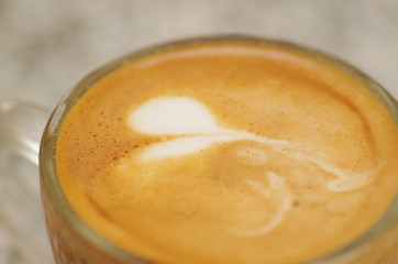Close up of coffee cup with latte art on top in ablurred background