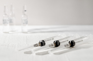 Three disposable medical syringes on a neutral background, closeup.