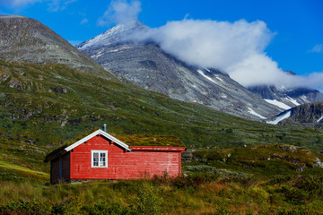 Fototapeta na wymiar Wooden cottage in the valley. Stone snowy mountains. Norway.