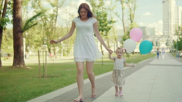 A young woman with a child is walking in the park with balloons