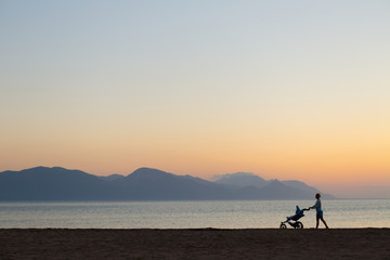 Silhouette of mother with stroller enjoying motherhood at sunset landscape