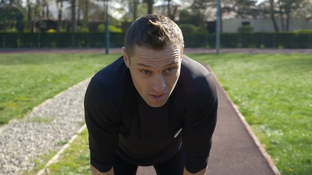 Closeup of tired young athlete in tracksuit stopping to rest after jogging in the park then starting to run
