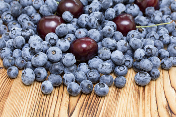 Natural bright background of natural fresh ripe blueberries and cherries  on brushed wooden table