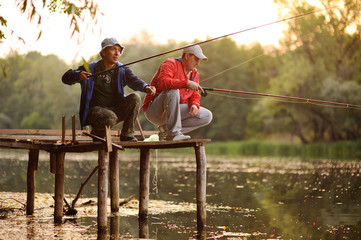 Two fishermen with fishing rods catching fish in the river standing on the pier bridge