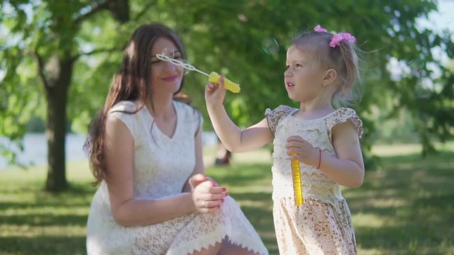 A little girl with her mom is blowing soap bubbles in the park