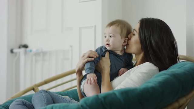 Medium shot of mother sitting in papasan chair whispering to baby son / Provo, Utah, United States