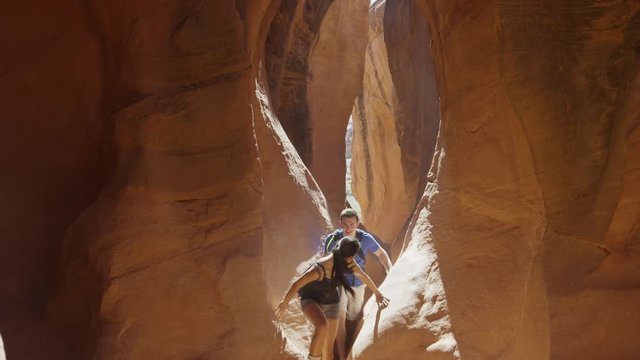 Wide slow motion panning shot of couple hiking in narrow slot canyon / Escalante, Utah, United States