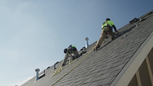 Wide panning low angle shot of workers installing parts on roof / Mapleton, Utah, United States