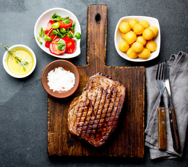 Grilled beef steak served on wooden table with tomato salad and potatoes balls. Barbecue, bbq meat beef tenderloin. Top view, slate background