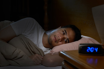 Depressed man suffering from insomnia lying in bed