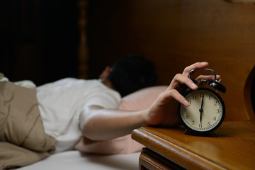 Young man turning off the alarm clock on the bed