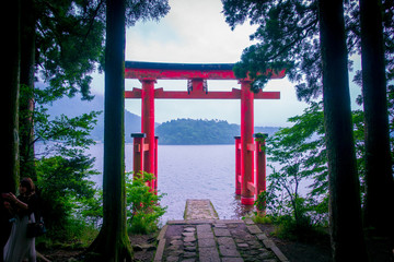 Bright red Torii gate submerged in the waters of Ashi lake, caldera with mountains on the...
