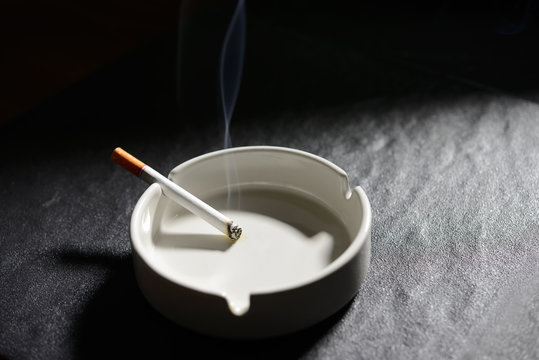 Lit cigarette lying on an empty white ashtray