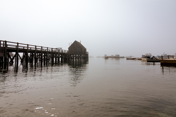 Dock house and boats in the harbor as the morning fog slowly fades away