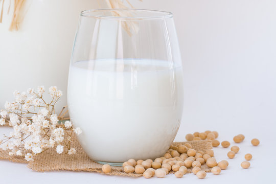 Soy milk in a glass and a pitcher with raw soybean seeds  on white table.
