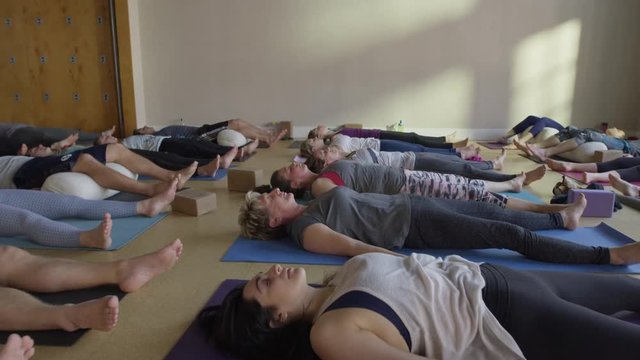 Medium slow motion zoom out shot of yoga students in corpse pose / Provo, Utah, United States