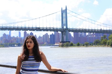 Woman in blue dress standing by waterfront and bridge