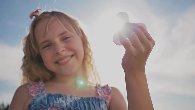 A young bright girl shows a spinner against the background of the sun's rays.