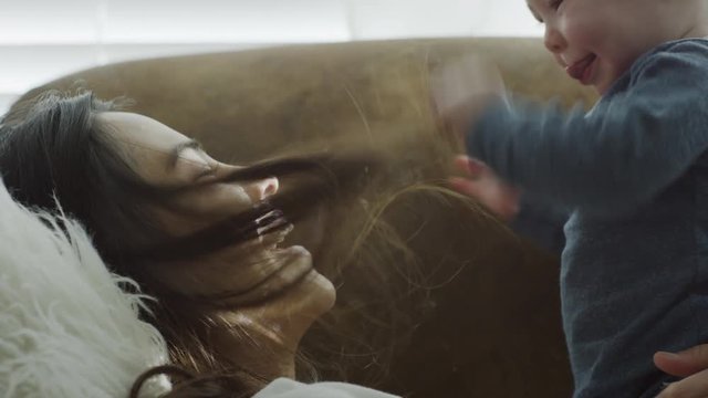 Close up of baby son pulling hair of mother on sofa / Provo, Utah, United States
