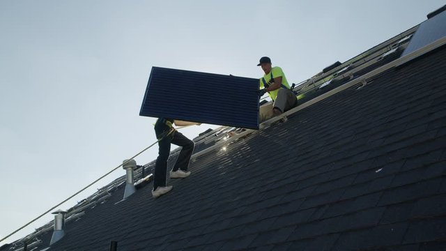 Wide panning low angle shot of workers carrying solar panel on roof / Mapleton, Utah, United States