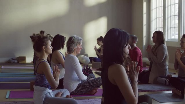 Medium slow motion panning shot of yoga class in prayer pose / Provo, Utah, United States