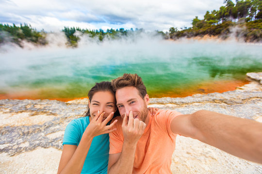 Funny selfie couple tourists at New Zealand pools travel. Young people doing goofy face at smell bad sulfur smell at colorful geothermal hot springs ponds, waiotapu.