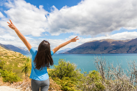 New Zealand travel happy tourist woman with arms up at Wanaka lake nature landscape outdoors. Wanderlust adventure young girl with peace hand sign.