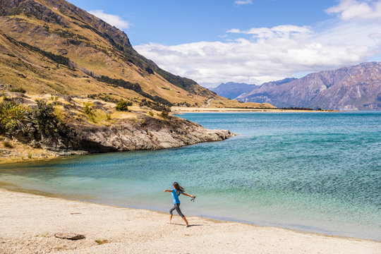 New Zealand travel happy tourist woman running of joy and freedom at beach shore of lake Hawea nature landscape. Near Wanaka, Otago Region