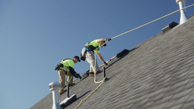 Wide panning low angle shot of workers on roof checking safety lines / Mapleton, Utah, United States