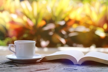 Open book and coffee cup on table closeup outdoor green nature blur background