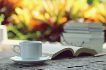 Open book and coffee cup on table closeup outdoor green nature blur background