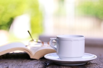 Open book and coffee cup on table closeup outdoor green nature blur background