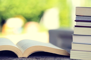 Open book and pile of books on table closeup outdoor green nature blur background